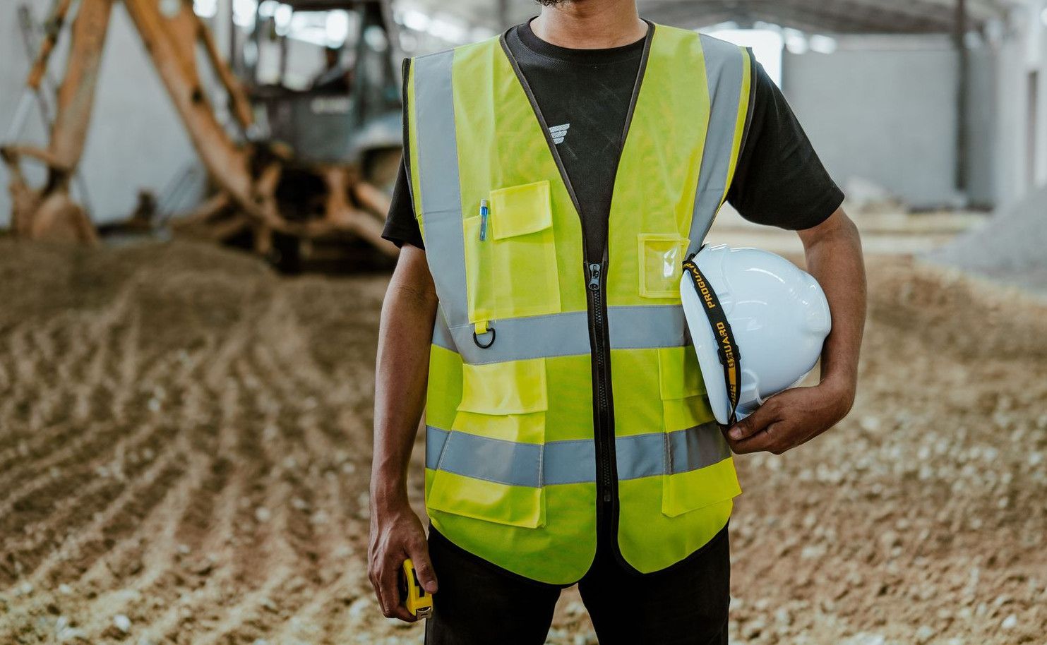 Portrait of a construction worker in safety gear holding a helmet inside an industrial setting.